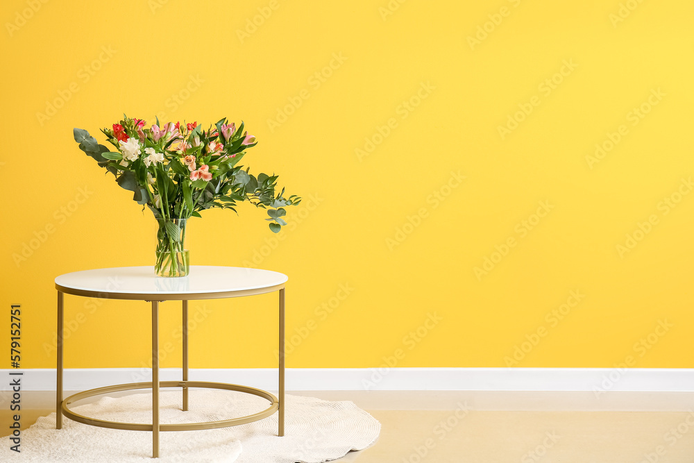 Vase with beautiful alstroemeria flowers on table near yellow wall