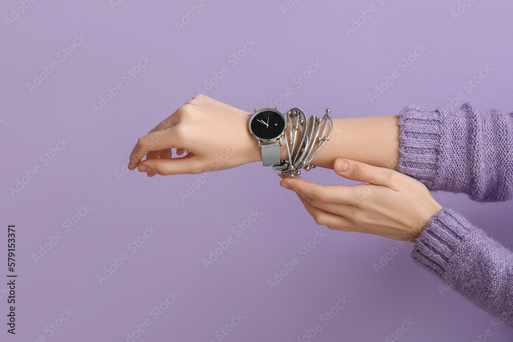 Woman with stylish wristwatch and bracelet on lilac background