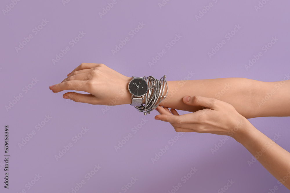 Woman with stylish wristwatch and bracelet on lilac background