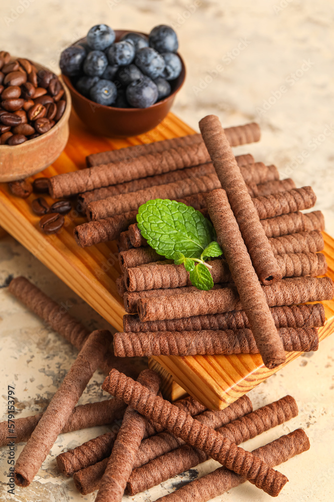 Board with delicious chocolate wafer rolls, blueberries and coffee beans on beige background