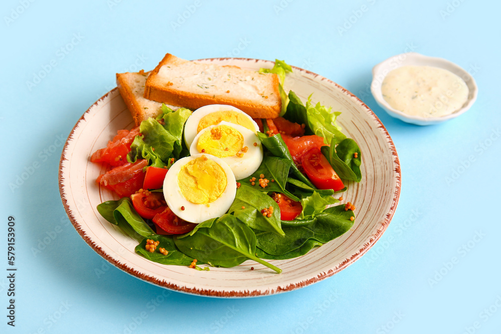 Plate of delicious salad with boiled eggs and salmon on blue background