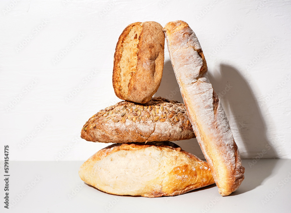 Loaves of different bread on table white wall