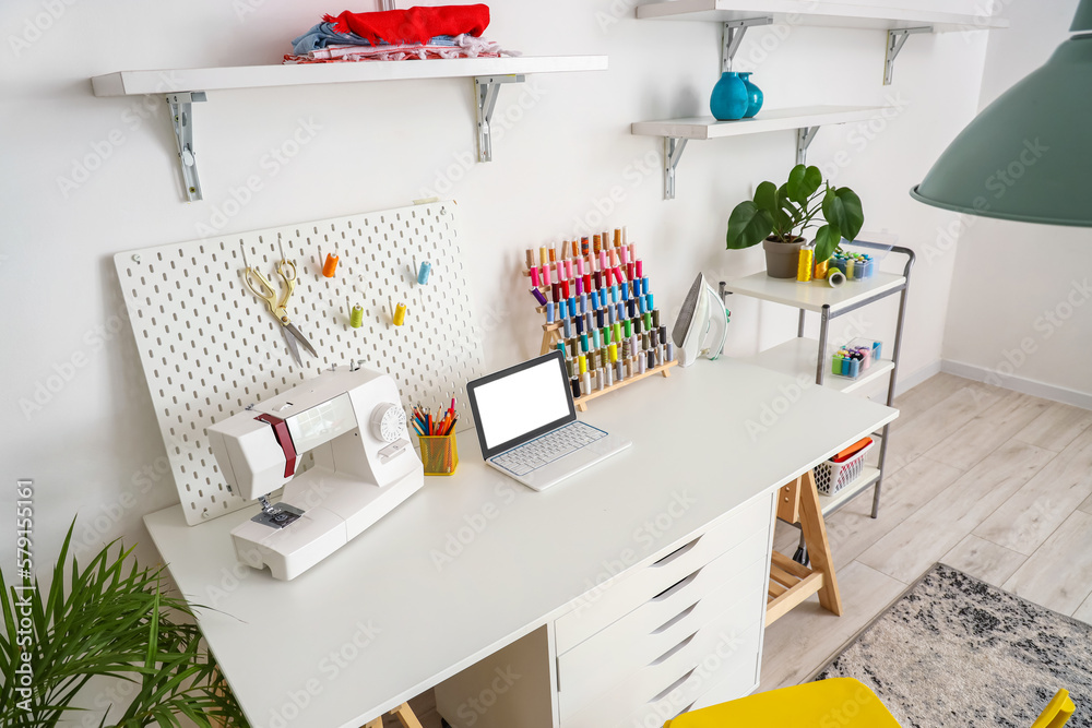 Tailors workplace with laptop, sewing machine and pegboard in atelier