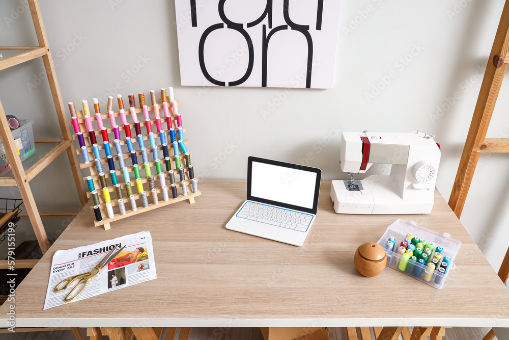 Tailors workplace with laptop, sewing machine and thread spools in atelier