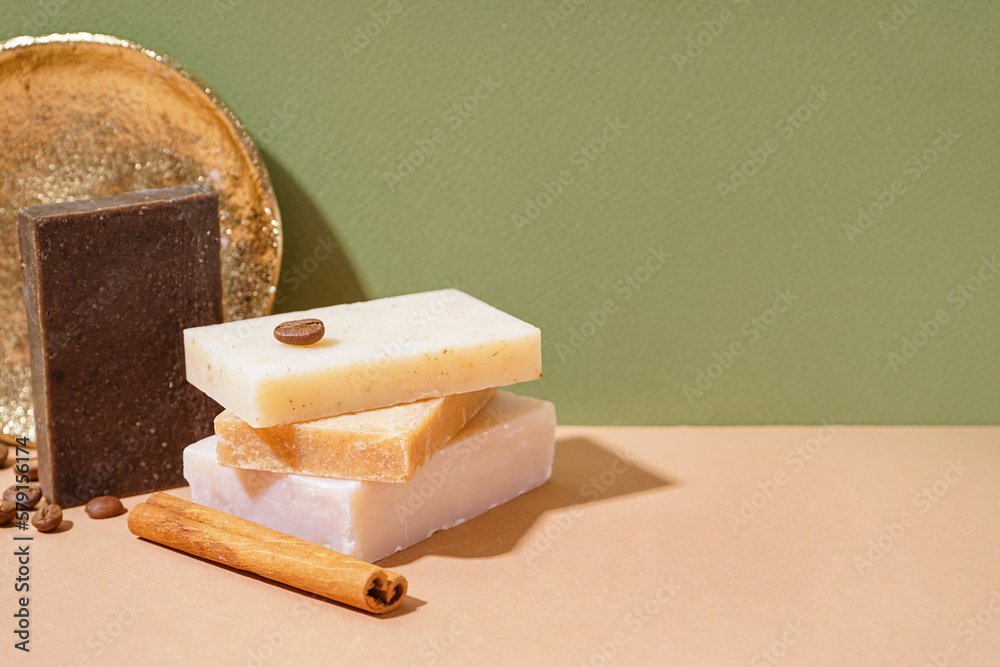 Stack of natural soap bars, coffee beans and cinnamon on color table