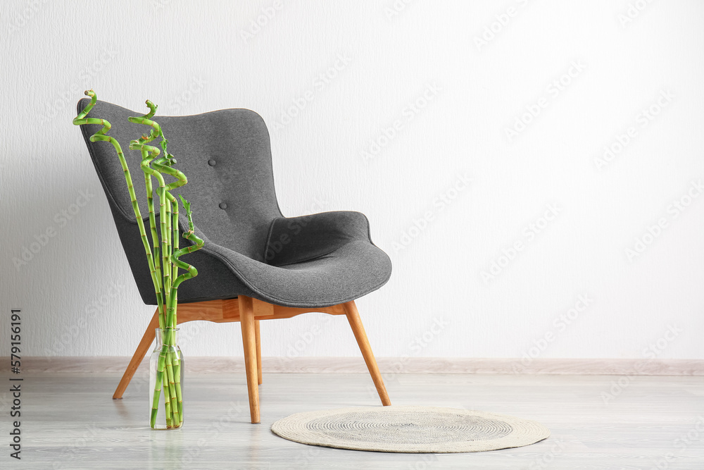 Vase with bamboo plant and armchair near white wall