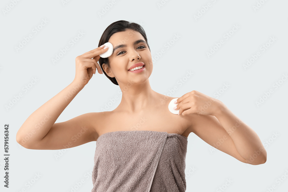 Young woman removing makeup with cotton pads on light background