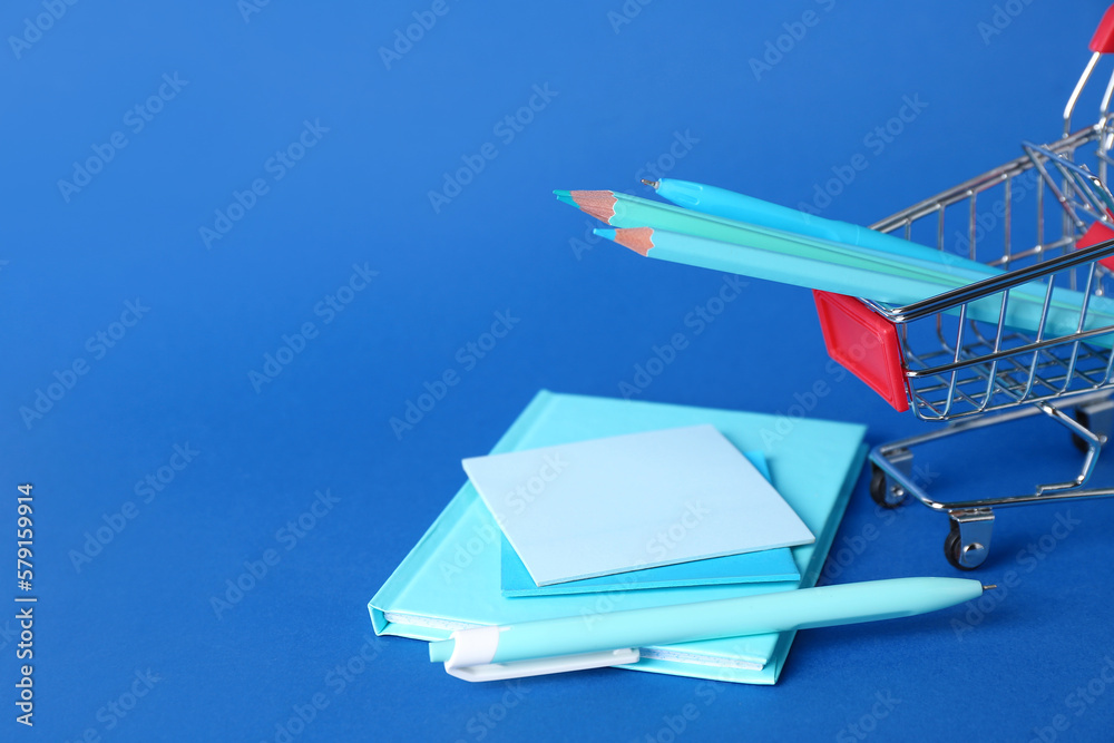 Shopping cart with stationery on blue background