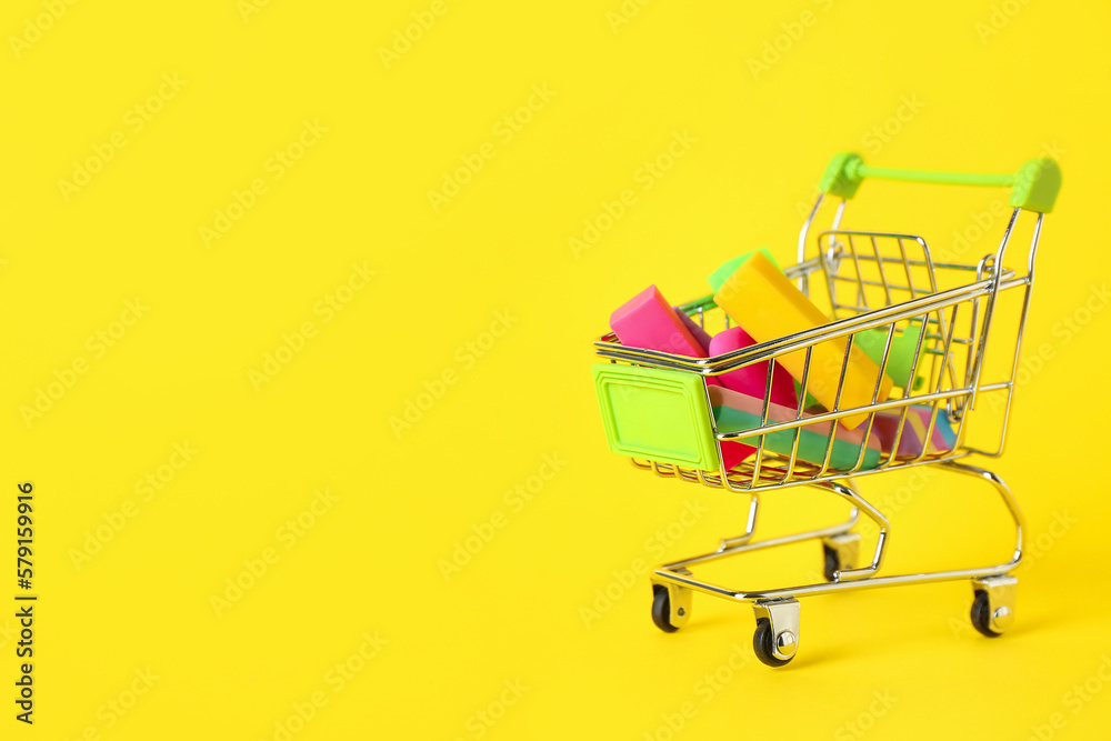 Shopping cart with erasers and chalk on yellow background