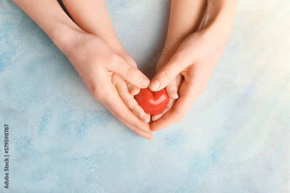 Hands of woman and child with red heart on light background. Mothers Day