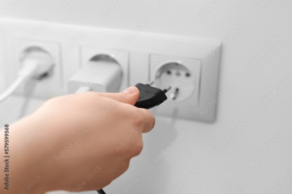 Woman putting plug into socket at home, closeup