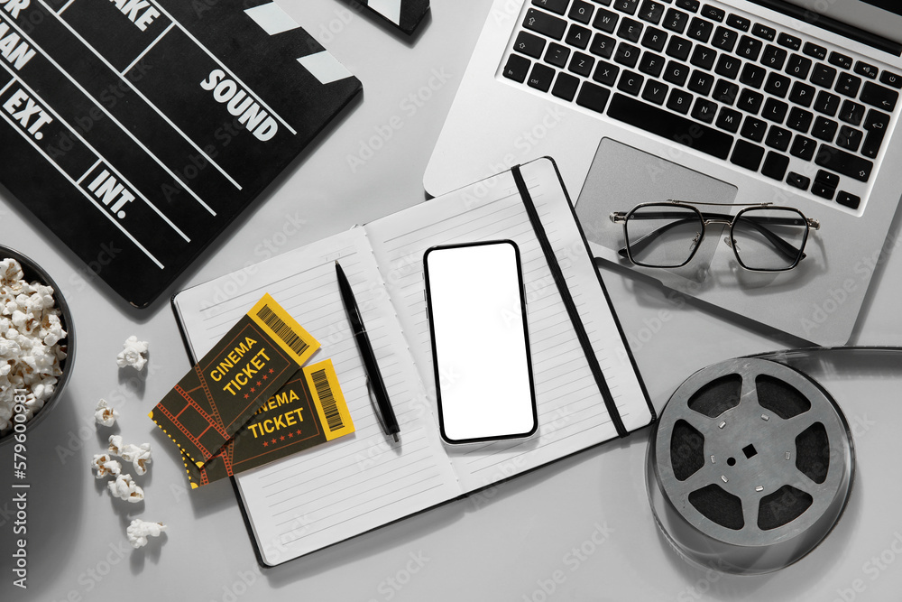 Movie clapper with mobile phone, laptop, reel, eyeglasses and notebook on grey background