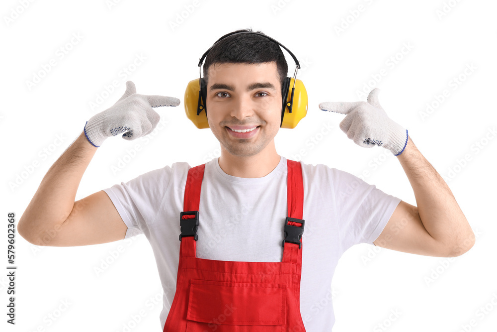 Young carpenter pointing at hearing protectors on white background