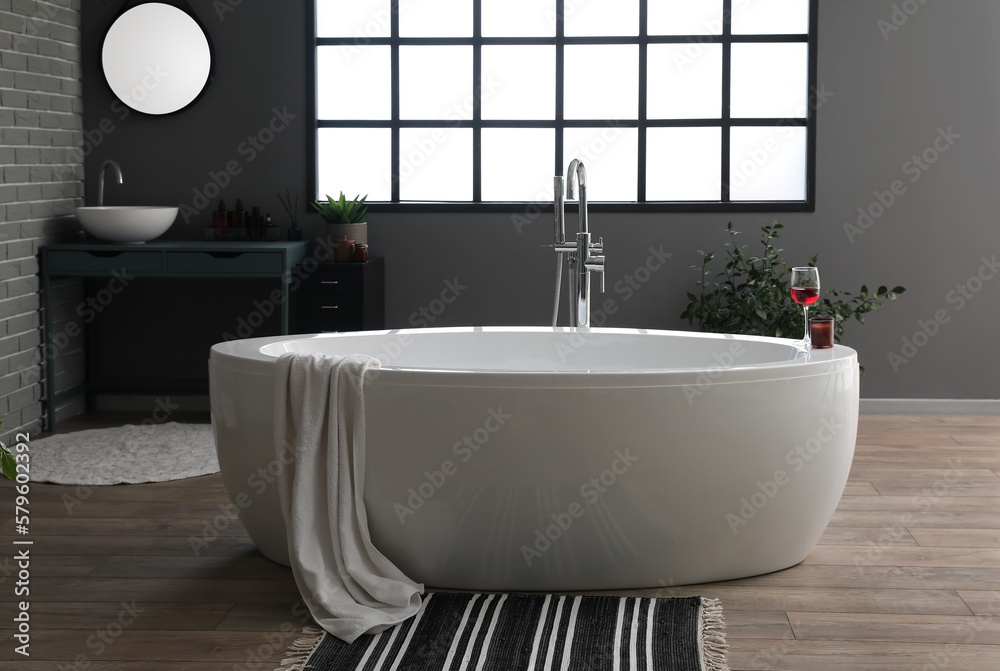 Bathtub with wine glass and candle in interior of modern bathroom