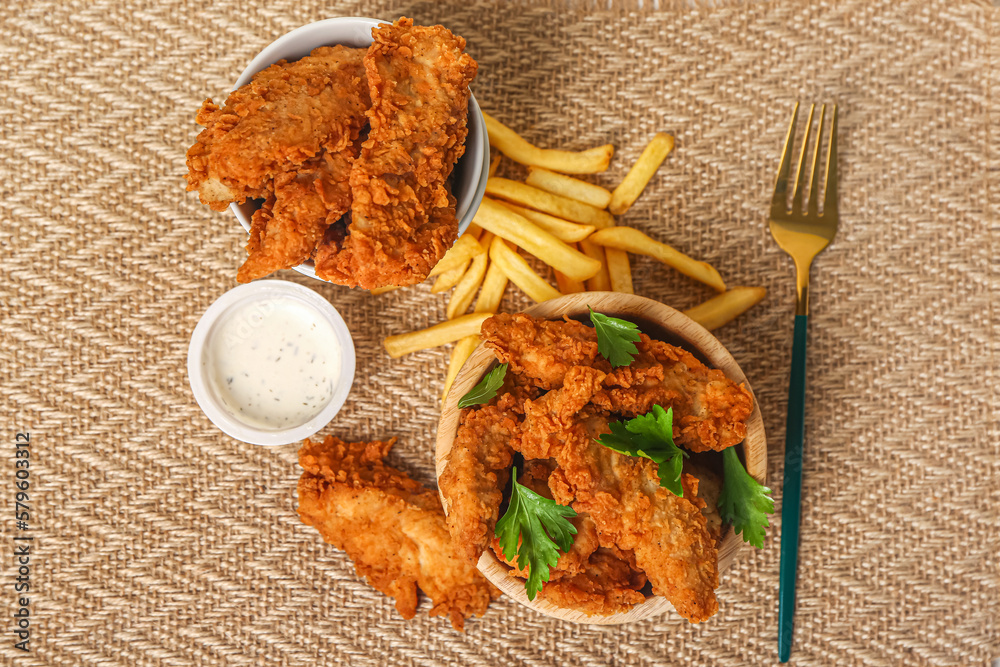 Bowls of tasty nuggets, french fries and sauce on fabric background