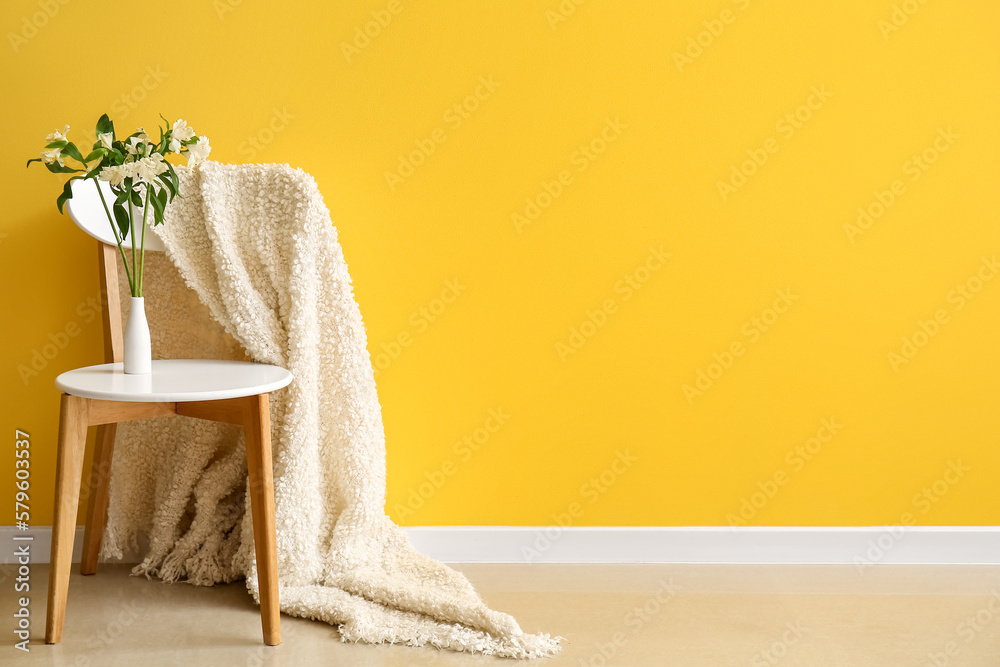 Vase with beautiful alstroemeria flowers on stool near yellow wall