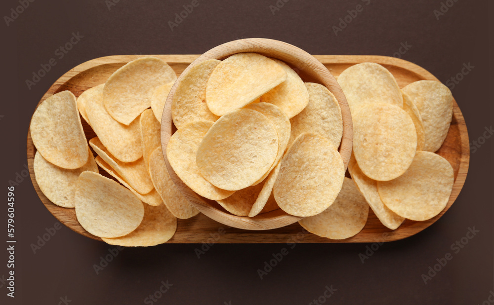 Board and bowl with delicious potato chips on brown background