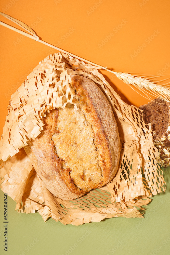 Parchment with fresh loaf of bread and wheat ear on green table near orange wall