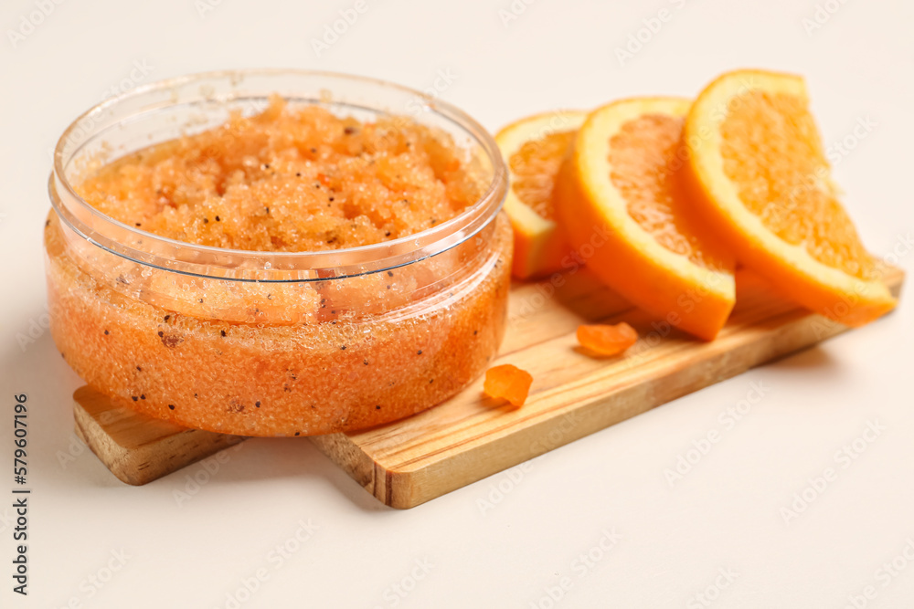 Wooden board with jar of natural body scrub and orange slices on light background, closeup