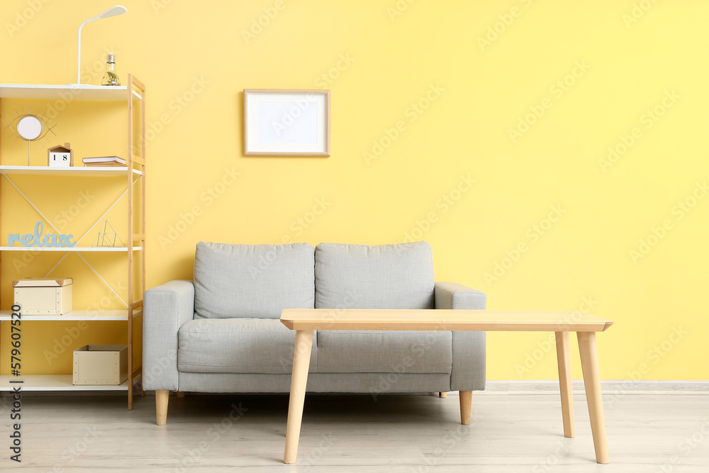 Interior of living room with stylish grey sofa near yellow wall