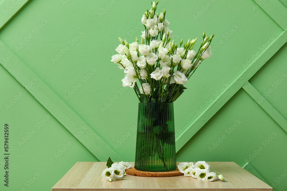 Vase with beautiful eustoma flowers on table near green wall