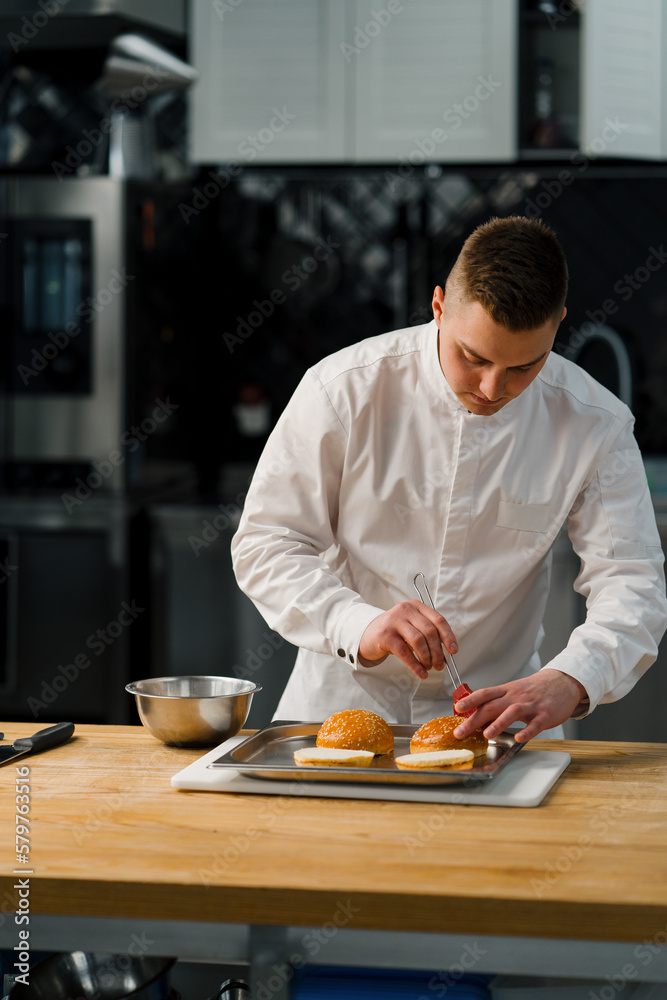 A chef butters burger buns with a brush in a professional kitchen gastronomy