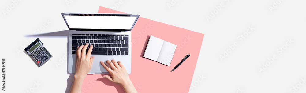 Person using a laptop computer with a notebook and a calculator