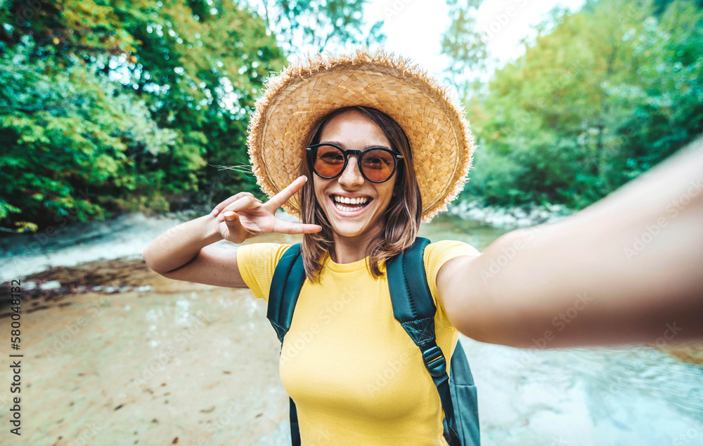 Happy female tourist with backpack taking selfie picture with smart mobile phone outside - Millenial