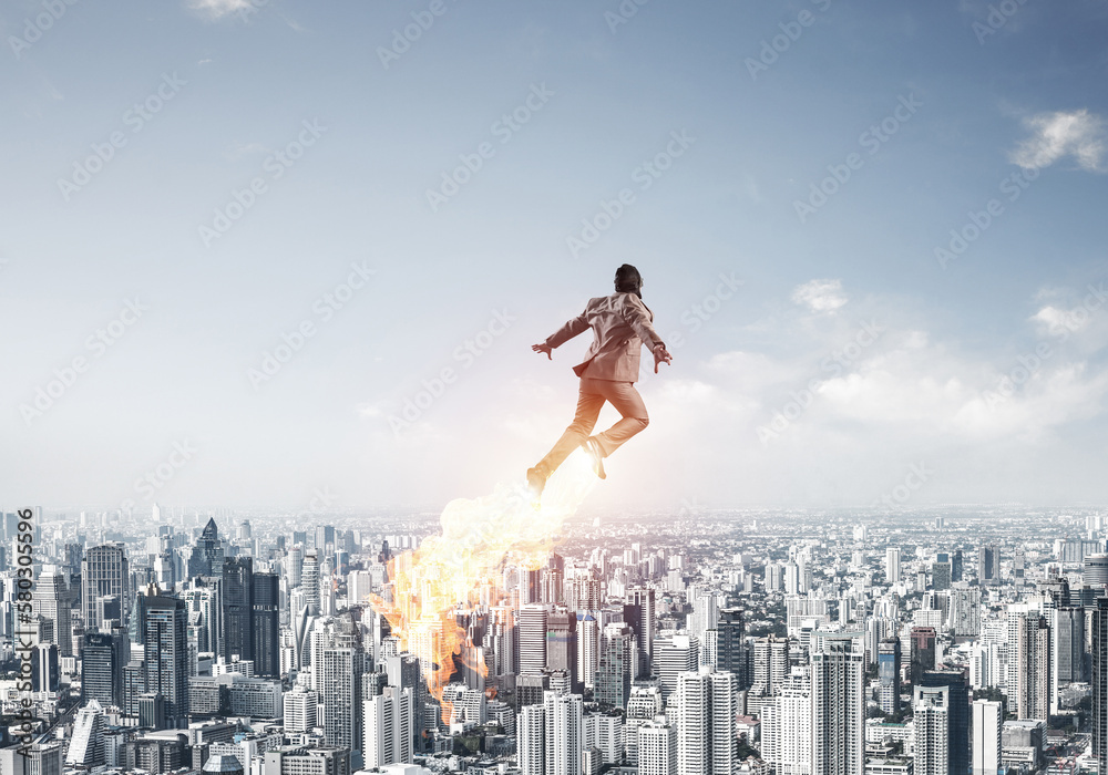 Businessman in suit and aviator hat flying in sky