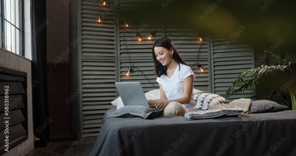 Smiling young Asian teen girl video calling on laptop. Happy mixed race pretty woman student looking