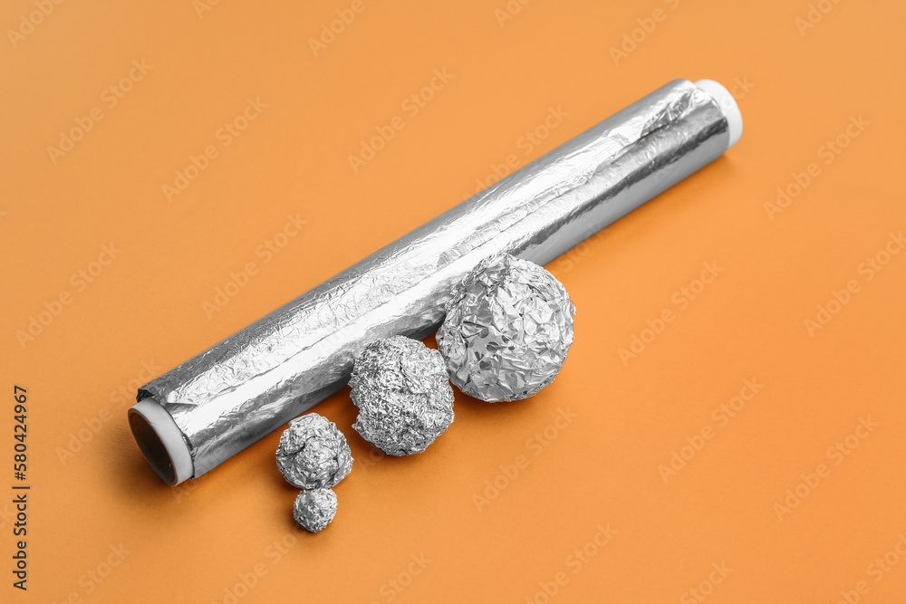 Roll and balls of aluminium foil on color background