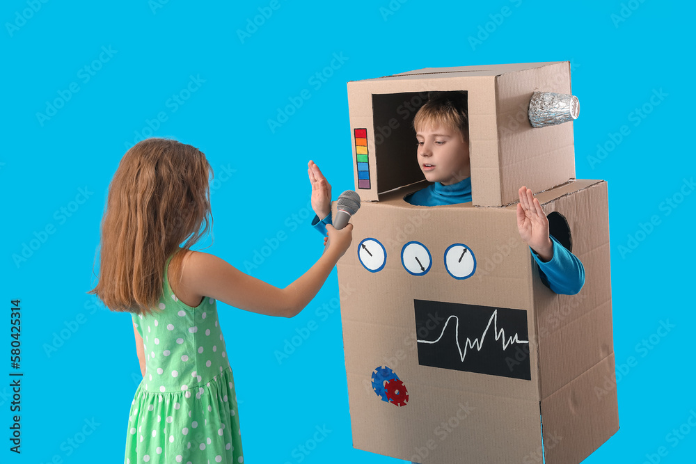 Little girl with microphone and boy in cardboard robot costume on blue background