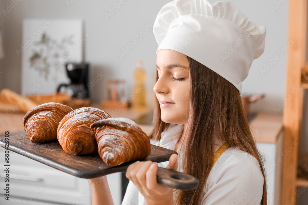 Little baker with board of tasty croissants in kitchen, closeup