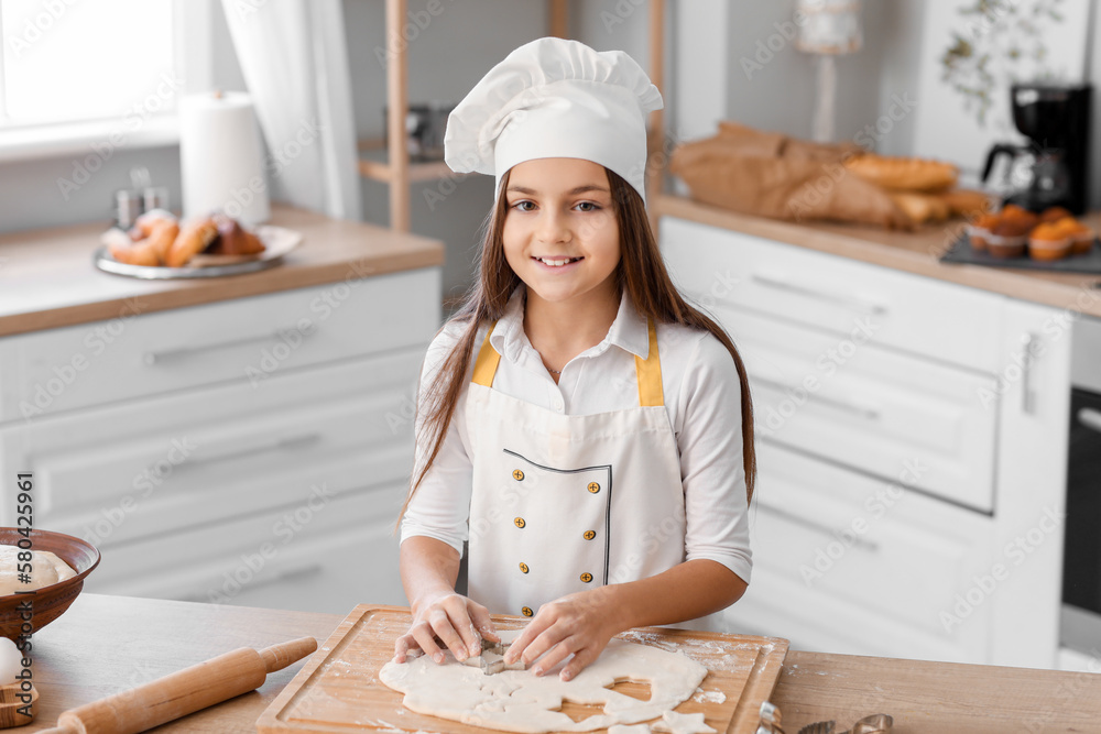 Little baker cutting dough for cookies in kitchen