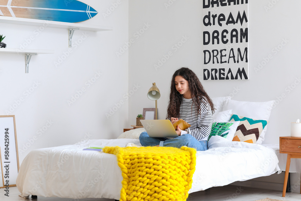 Female student with laptop studying online in bedroom