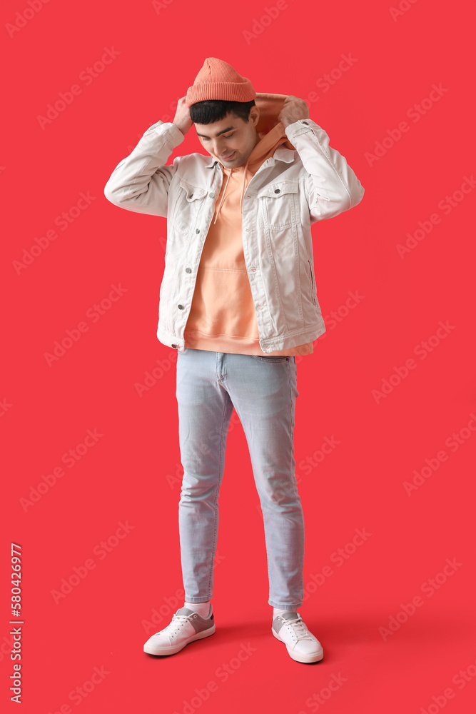 Stylish young man in beanie hat on red background