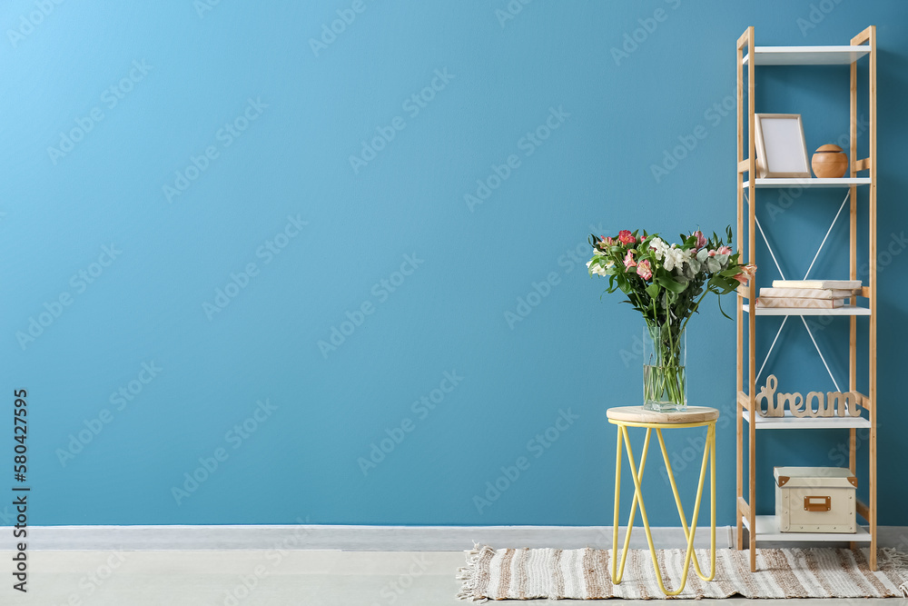 Vase with beautiful alstroemeria flowers on stool and shelving unit near blue wall