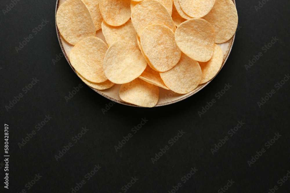 Plate with delicious potato chips on black background