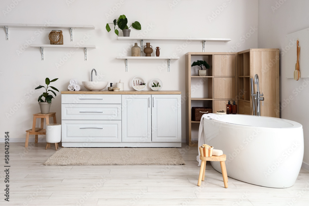 Interior of light bathroom with bathtub, counters and shelves