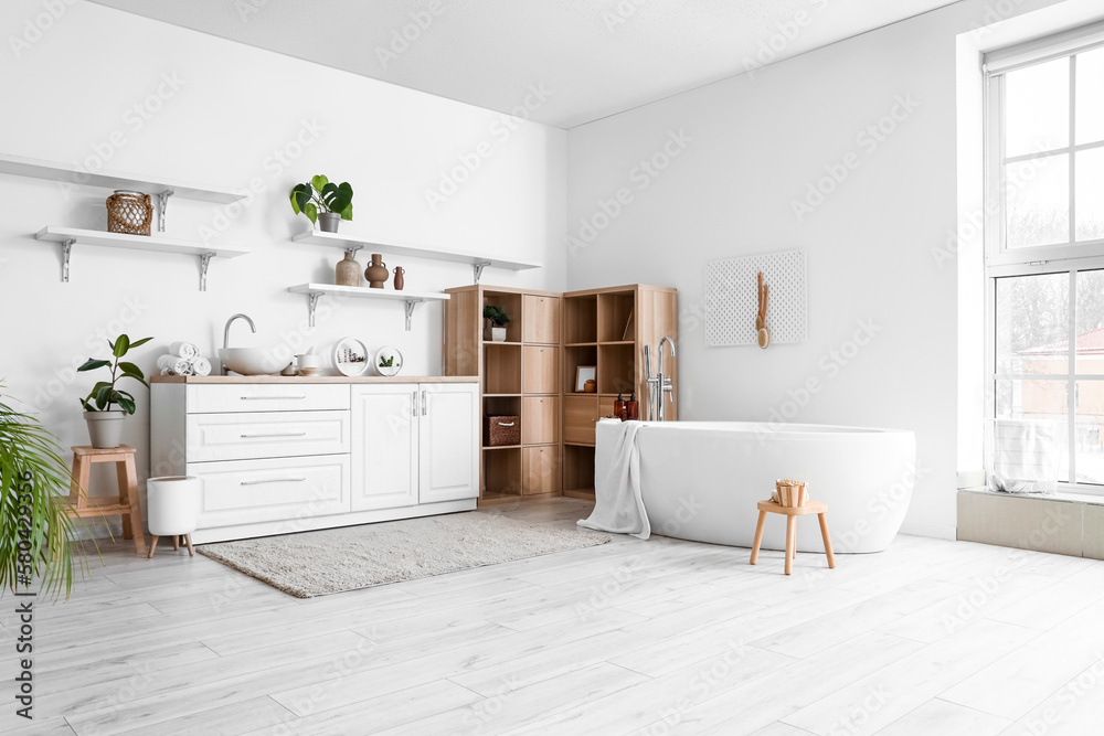 Interior of light bathroom with bathtub, counters and shelves