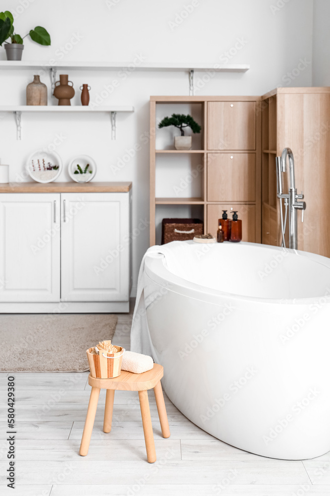 Interior of light bathroom with bathtub and shelves