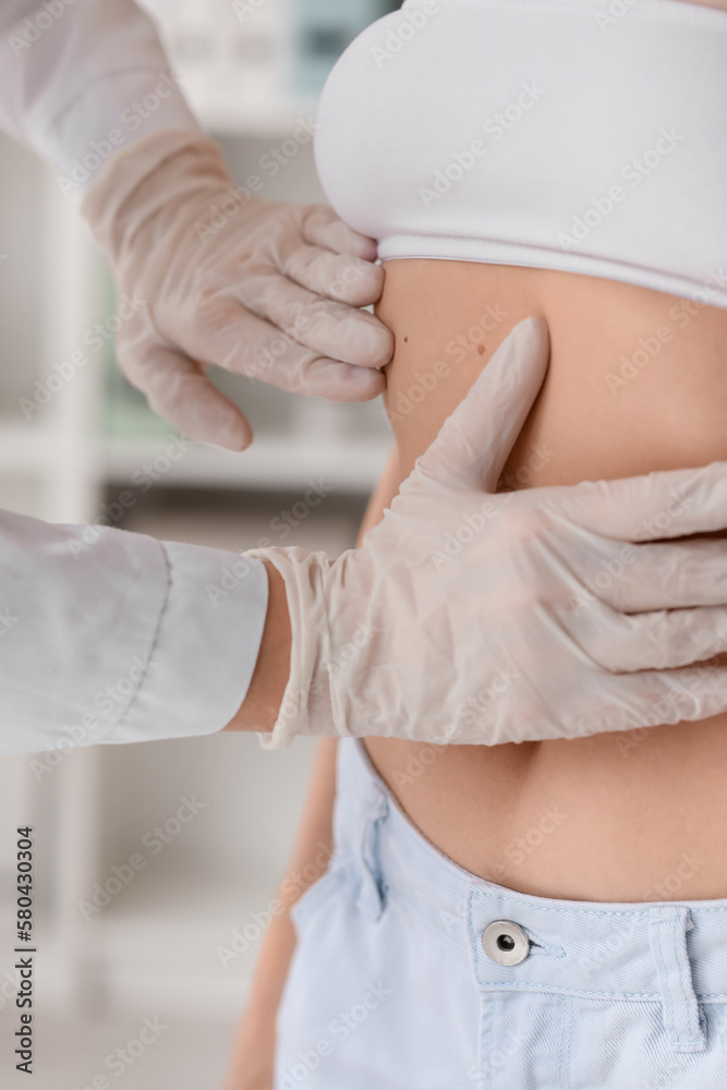 Dermatologist examining moles on young womans belly in clinic, closeup