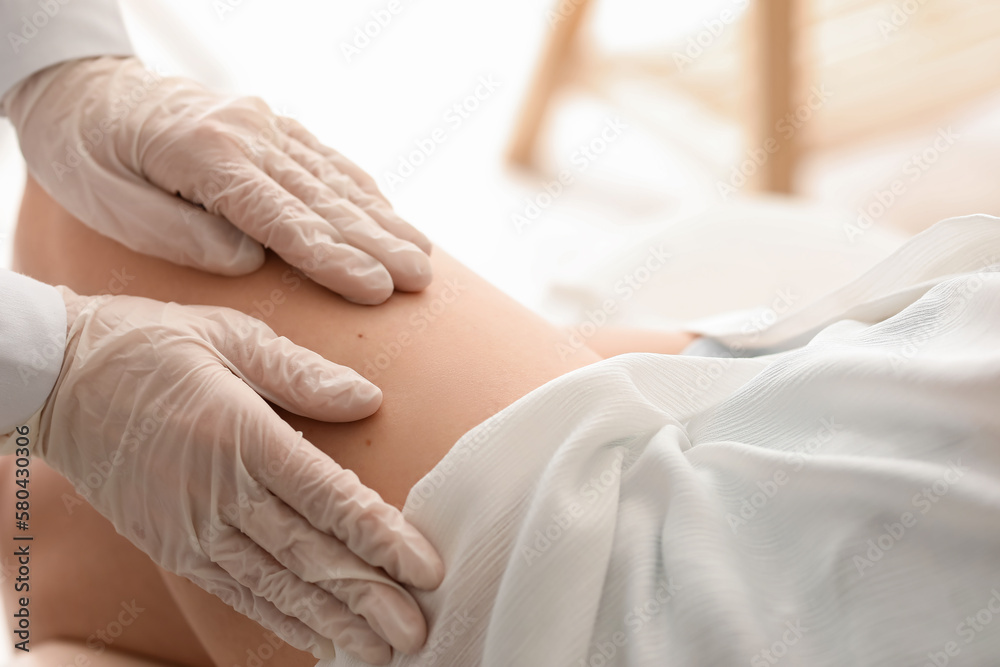 Dermatologist examining moles on young womans leg in clinic, closeup