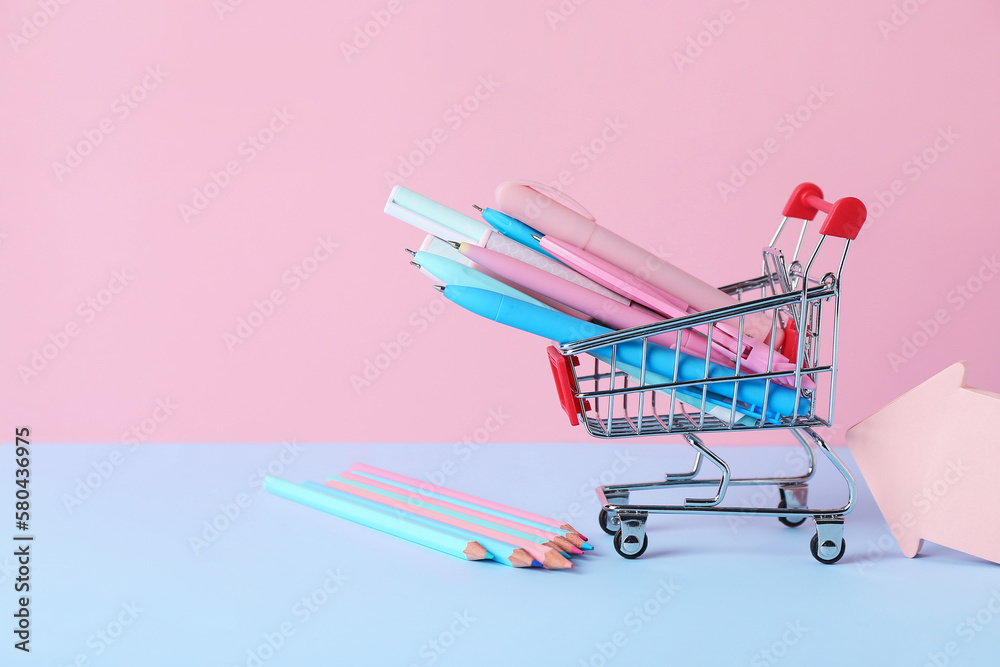 Shopping cart with different pens, pencils and sticky notes on color background