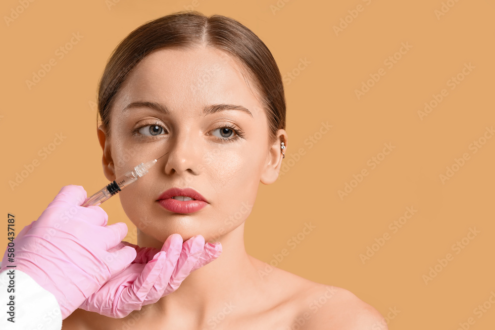 Young woman receiving filler injection in face against beige background