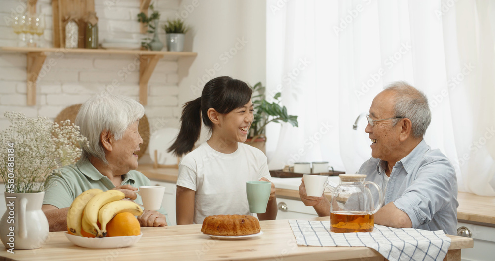 Asian pensioneer couple spending time with their granddaughter, drinking black tea, chatting and rel