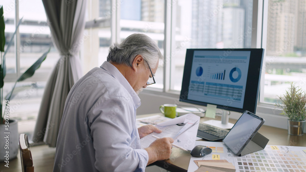 Asian senior mature man working with computers and tablet on table desk at home