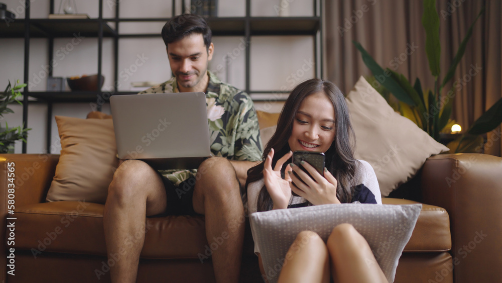 Couple sitting on the sofa on the phone and using laptop at home