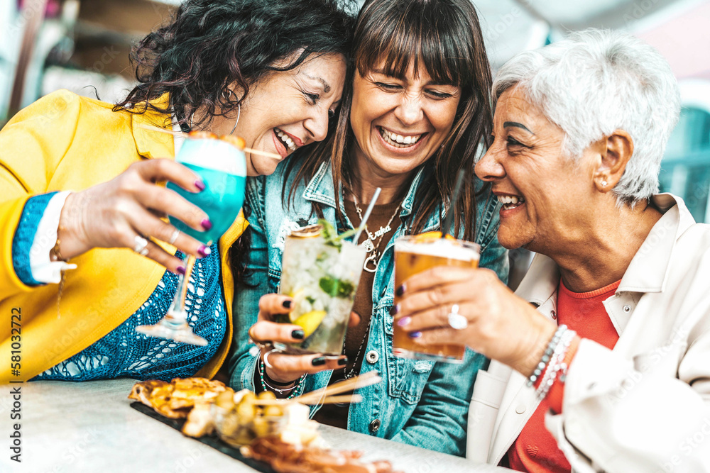 Happy senior women drinking cocktail glasses sitting at bar table - Group of best friends enjoying h