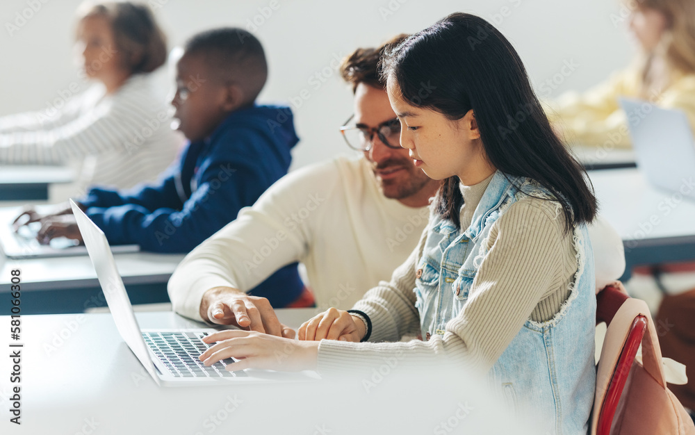 School educator providing assistance to a young student in a coding class